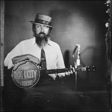 A person with a beard and a hat holding a banjo

Description automatically generated