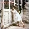 A young child in a white dress looking through a window

Description automatically generated