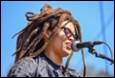 A person with dreadlocks singing into a microphone

Description automatically generated