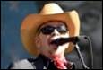 A person wearing a cowboy hat and sunglasses singing into a microphone

Description automatically generated