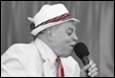 A person in a white suit and hat singing into a microphone

Description automatically generated with medium confidence