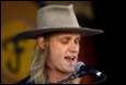 A person with long hair wearing a cowboy hat and a microphone

Description automatically generated with low confidence
