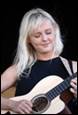 A person with blonde hair playing a guitar

Description automatically generated