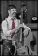 A person with a mustache and a red tie holding a bass

Description automatically generated