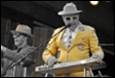 A person in a yellow suit and hat speaking into a microphone

Description automatically generated