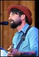 A person with a beard and a hat singing into a microphone

Description automatically generated