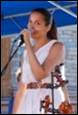 A person in a white dress singing into a microphone

Description automatically generated