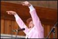 A person in pink shirt with arms raised in front of microphone

Description automatically generated