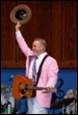 A person in a pink suit holding a hat and a guitar

Description automatically generated