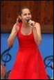 A person in a red dress singing into a microphone

Description automatically generated
