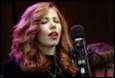 A person with red hair and red lipstick singing into a microphone

Description automatically generated