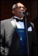 A person in a suit and bow tie singing into a microphone

Description automatically generated
