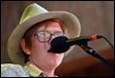 A person wearing a cowboy hat and glasses singing into a microphone

Description automatically generated