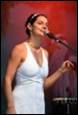 A person in a white dress singing into a microphone

Description automatically generated