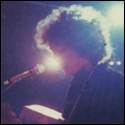 A person with curly hair singing into a microphone

Description automatically generated
