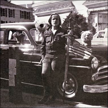 A person holding a sword and a flag next to a car

Description automatically generated