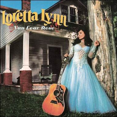 A person in a blue dress leaning against a tree with a guitar
Description automatically generated