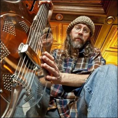 A person sitting on the floor playing a guitar
Description automatically generated