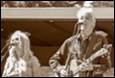 A person playing a guitar and a person standing next to him

Description automatically generated with low confidence