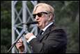 A person in a suit and tie speaking into a microphone

Description automatically generated with medium confidence