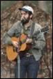 A person with a beard playing guitar

Description automatically generated