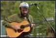 A person playing guitar and standing in front of a microphone

Description automatically generated