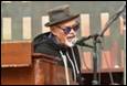 A person in a hat and sunglasses speaking into a microphone

Description automatically generated