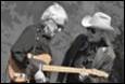 A person playing guitar with another person in cowboy hat

Description automatically generated