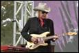 A person in a cowboy hat playing a guitar

Description automatically generated