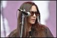 A person with long hair wearing sunglasses and a microphone

Description automatically generated