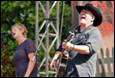 A person singing on stage with a person in the background

Description automatically generated