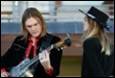 A person playing a guitar with a person in the background

Description automatically generated with medium confidence