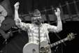 A person holding a guitar and raising his hands

Description automatically generated