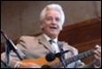 A person with a guitar in front of a microphone

Description automatically generated