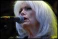 A person with white hair singing into a microphone

Description automatically generated