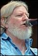 A person with a white beard and a microphone

Description automatically generated