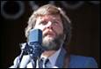 A person with a beard speaking into a microphone

Description automatically generated