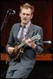 A person in a suit playing a guitar

Description automatically generated