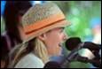 A person wearing a hat speaking into a microphone

Description automatically generated