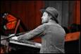 A person in a hat playing a piano

Description automatically generated