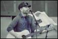 A person playing guitar and singing into a microphone

Description automatically generated