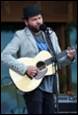 A person playing guitar and singing into a microphone

Description automatically generated