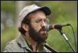 A person with a beard and a hat speaking into a microphone

Description automatically generated