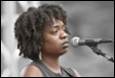 A person with curly hair speaking into a microphone

Description automatically generated