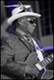 A person in a suit and hat playing a guitar

Description automatically generated with low confidence