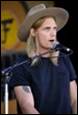 A person with long hair wearing a cowboy hat and a microphone

Description automatically generated with low confidence