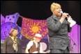 A person singing into a microphone on a stage

Description automatically generated with medium confidence