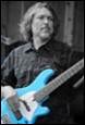 A person with a mustache playing a blue guitar

Description automatically generated