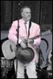 A person in a pink suit playing a guitar

Description automatically generated
