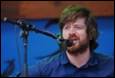 A person with a beard singing into a microphone

Description automatically generated
